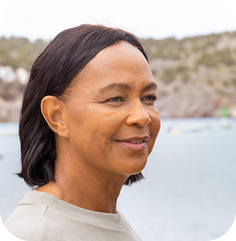 A woman smiling with water in the background after visiting us for earwax removal in Markham, Ontario
