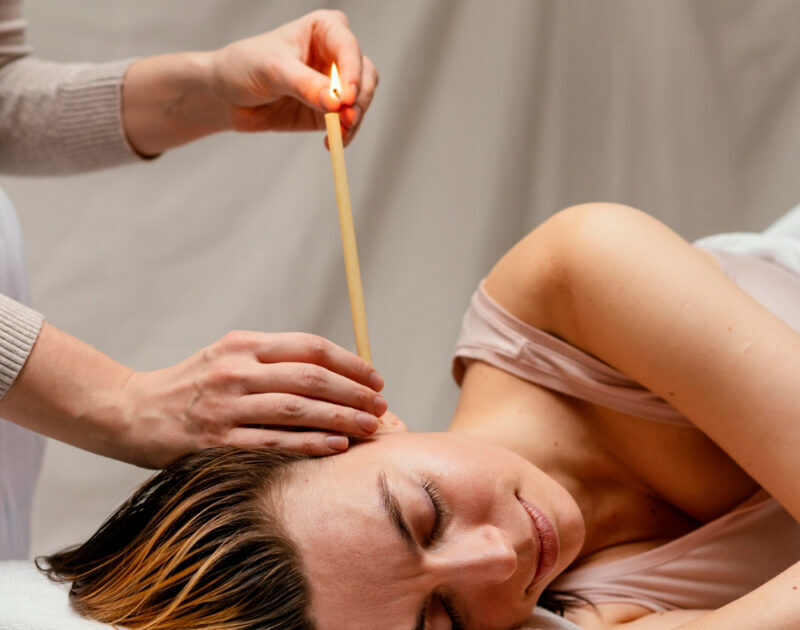A woman lying on her side receiving ear candling treatment