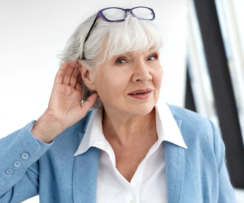 An older woman with white hair with her hand to her hear for a blog post on hearing loss and dementia