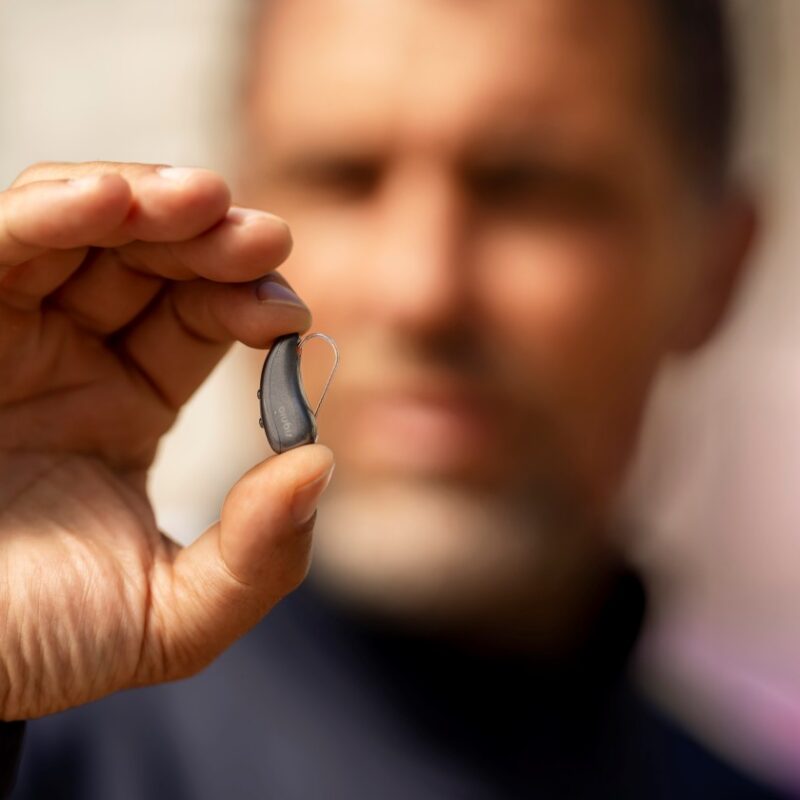 A man holding up a hearing aid for a blog post about When to Get Hearing Aids: Is Earlier Better?